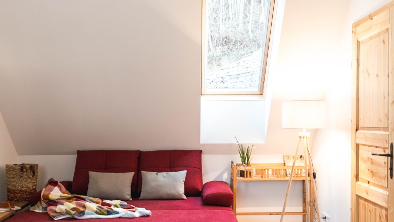 Gem&uuml;tliches Wohnzimmer mit rotem Sofa, Deckenleuchte und Dachfenster.