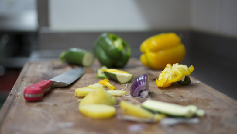Gemüse und Messer auf einem Schneidebrett in einer Küche.