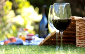 Zwei Weingl&auml;ser und ein Picknickkorb auf einer Wiese.