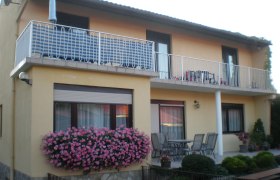 Zweist&ouml;ckiges Haus mit Balkon, Blumen und Gartenm&ouml;beln.