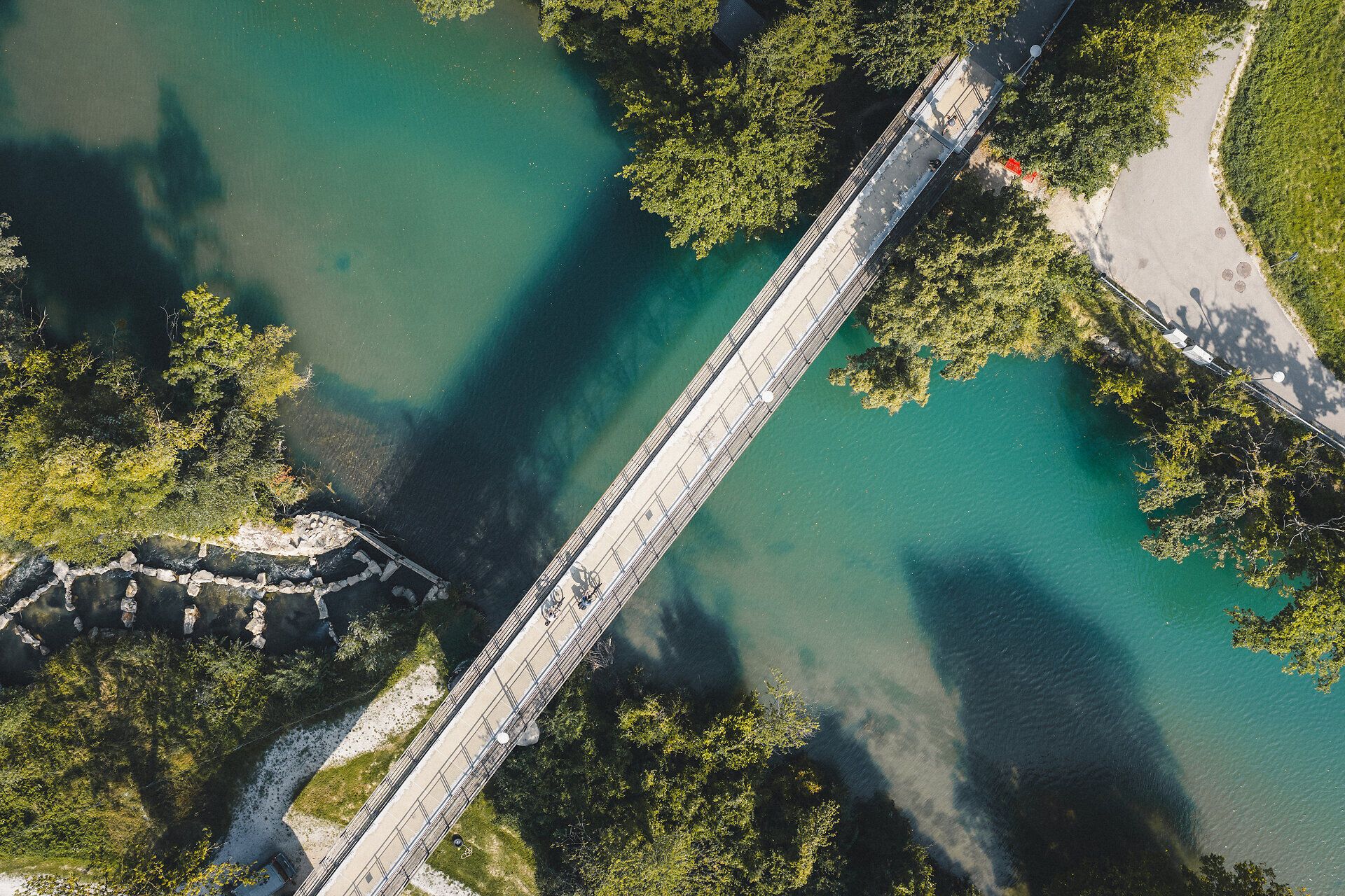 Zwei Radfahrer fahren auf einem Radweg über eine Brücke, darunter die tiefblaue Erlauf und Bäume entlang des Ufers.