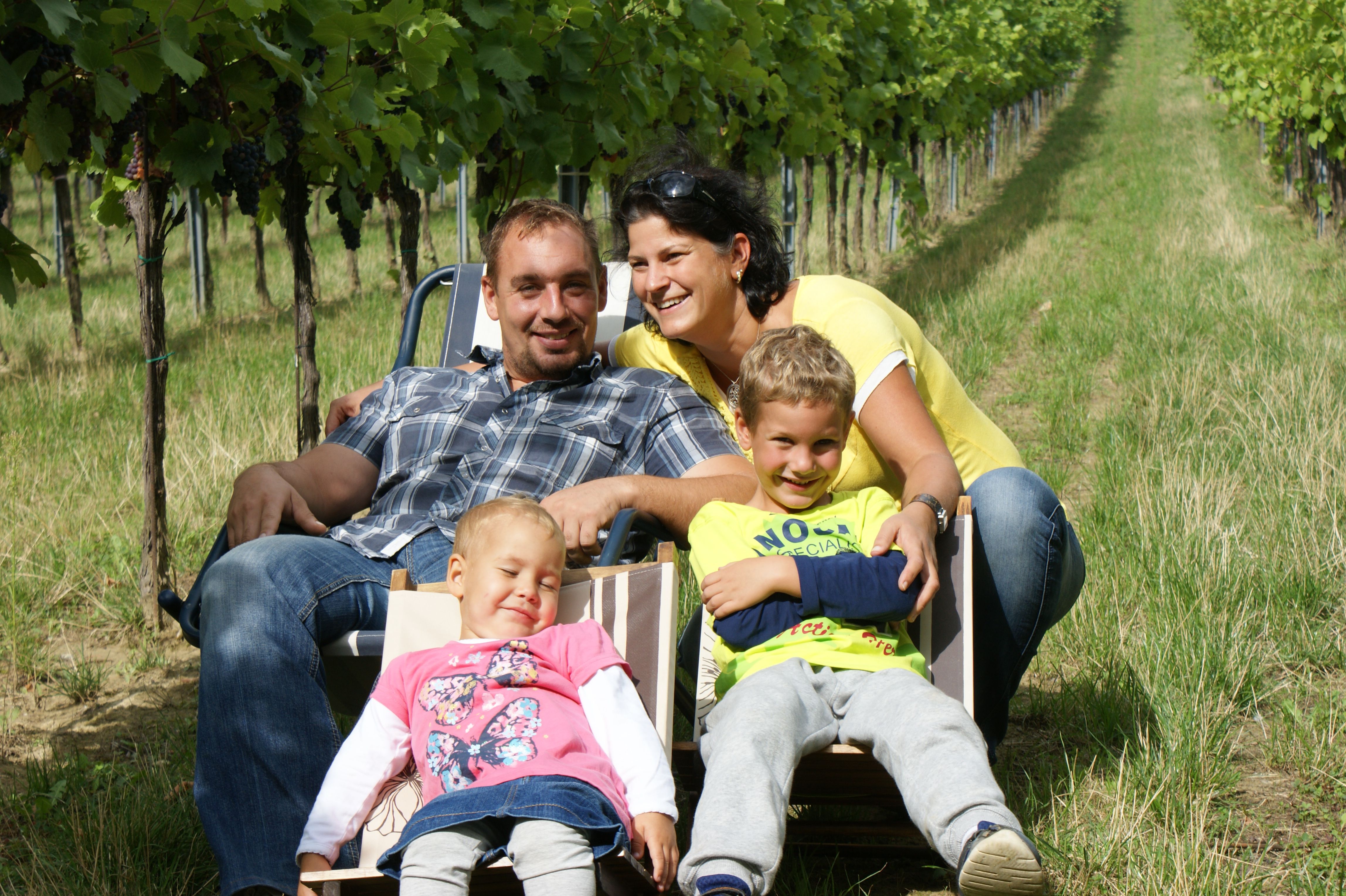 Familie sitzt auf Liegestühlen in einem Weinberg.
