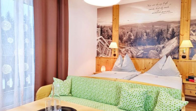 Gemütliches Doppelzimmer mit zwei Betten, grünem Sofa und großem Wandbild einer Landschaft.