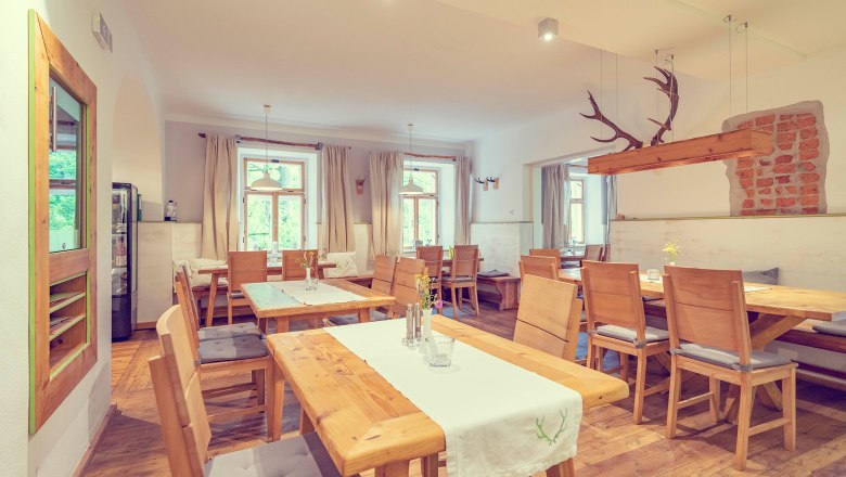 Ein rustikal-moderner Raum mit Holzm&ouml;beln, wei&szlig;en W&auml;nden und gro&szlig;en Fenstern. Ein Geweih h&auml;ngt als Dekoration von der Decke.