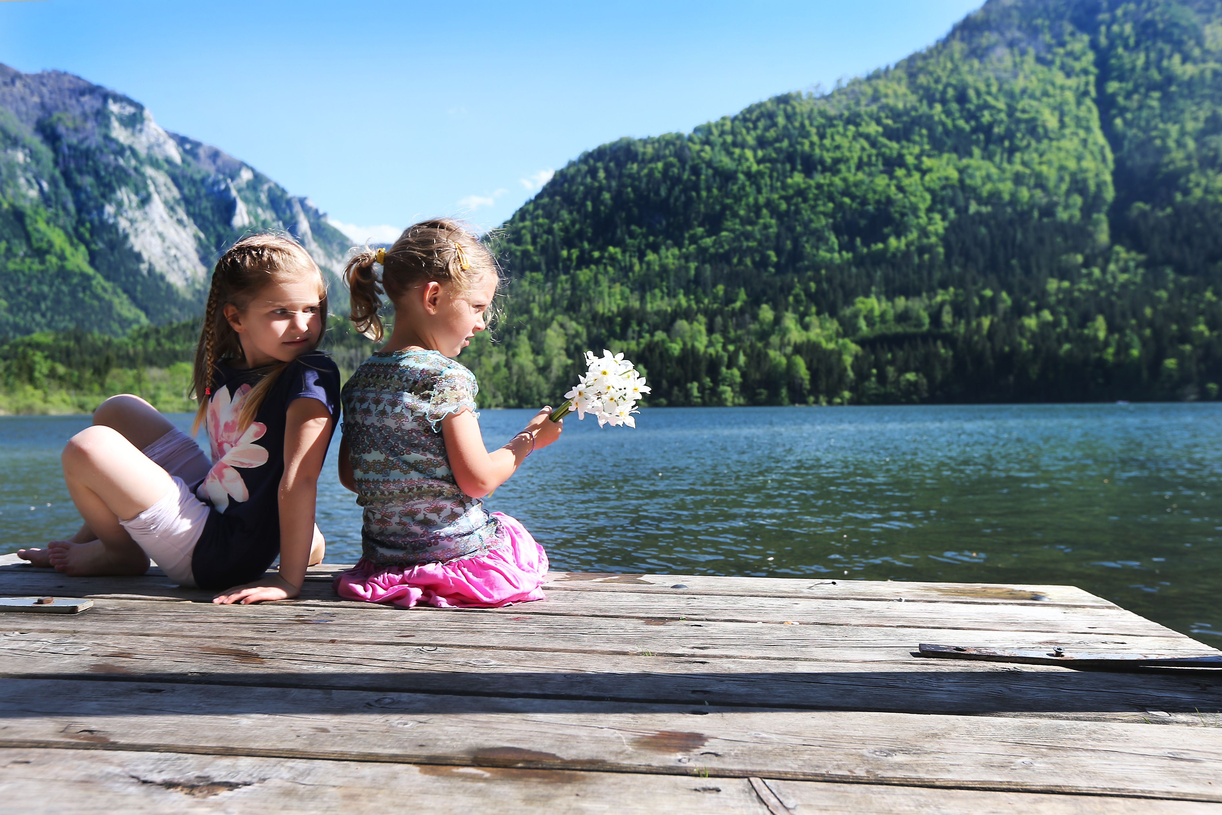 Zwei Kinder sitzen auf einem Steg am Lunzer See mit Bergen im Hintergrund.