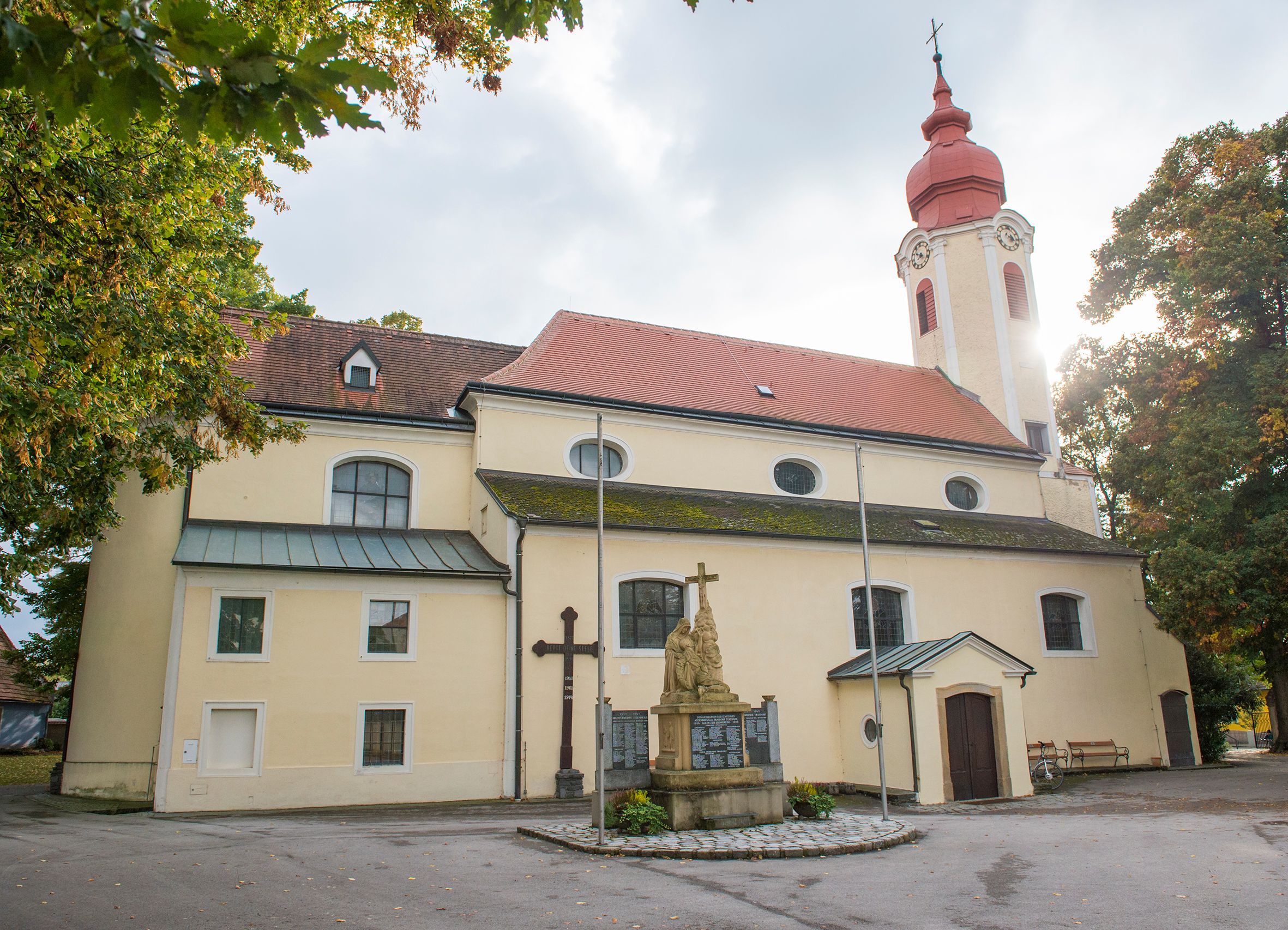 Pfarrkirche Heiligeneich mit Statue und Kreuz im Vordergrund.