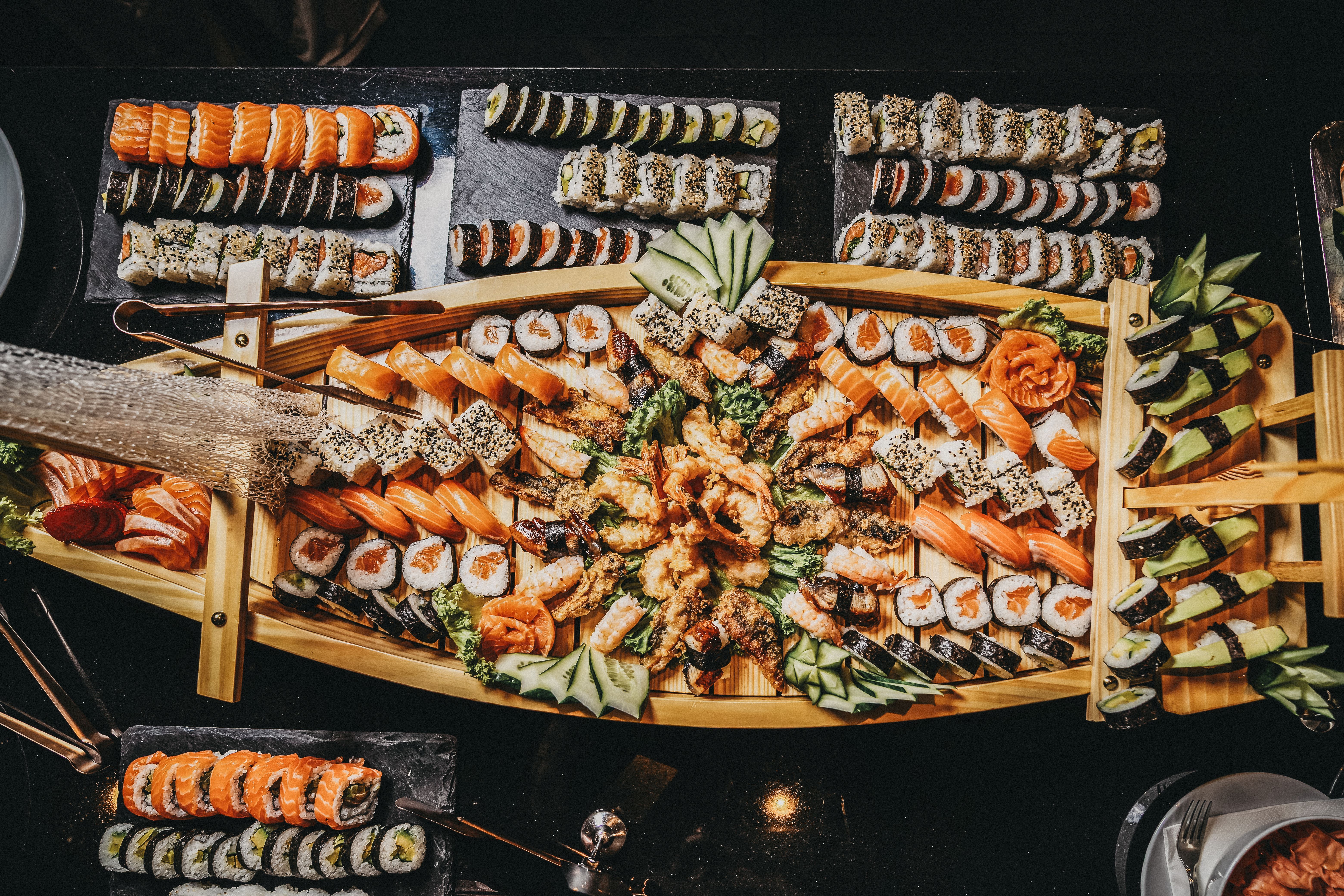 Ein großes Sushi-Buffet auf einem Holztablett mit verschiedenen Sushi-Varianten, dekoriert mit Gurken und Ingwer.