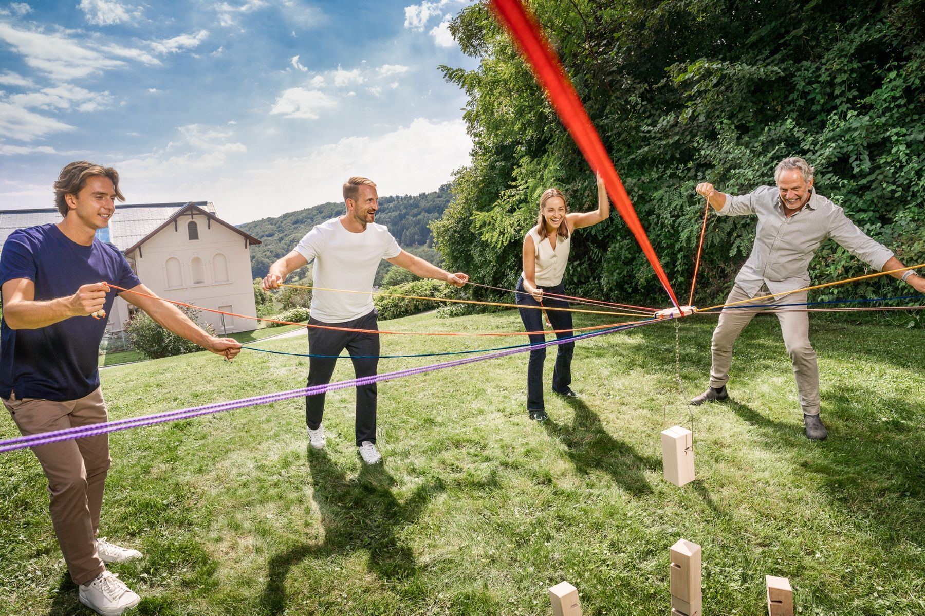 Vier Personen bei einem Teambuilding Spiel mit bunten Bändern auf einer Wiese vor dem Seminarhotel Refugium Hochstrass