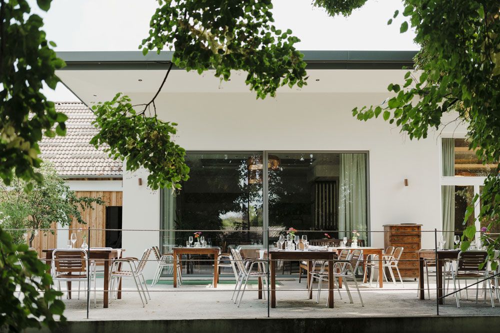 Terrasse mit Tischen und Stühlen, umgeben von grünen Bäumen.