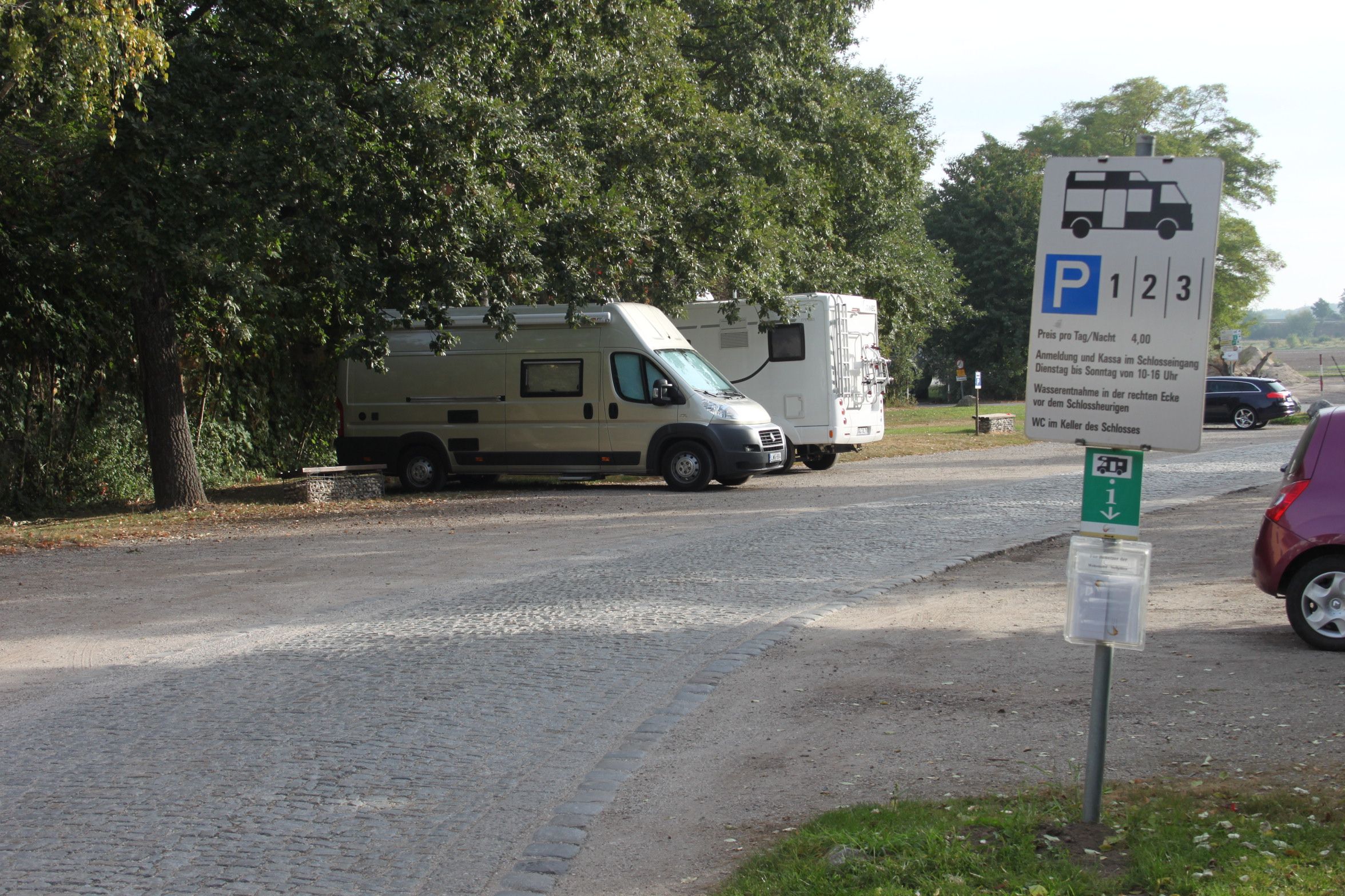 Wohnmobilstellplatz mit zwei geparkten Wohnmobilen und einem Hinweisschild.