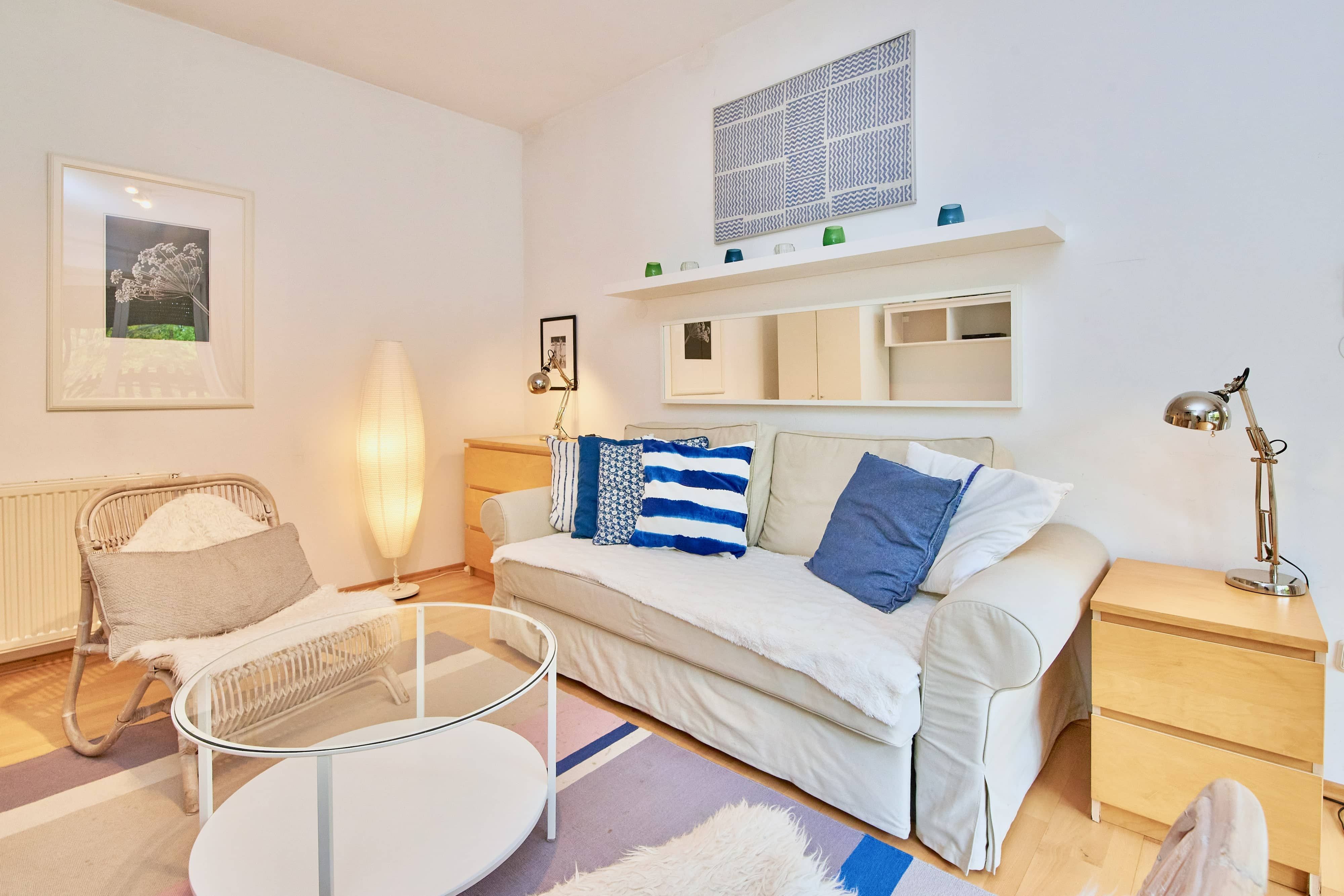 Gemütliches Wohnzimmer mit Sofa, Kissen, Sessel, Stehlampe und Couchtisch.