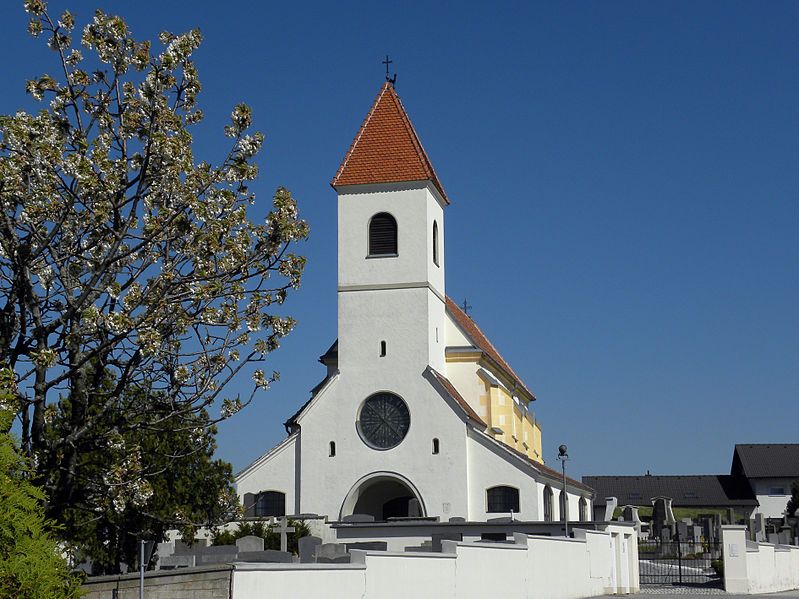 St. Anna Kirche in Wiesmath mit blauem Himmel und blühendem Baum im Vordergrund.