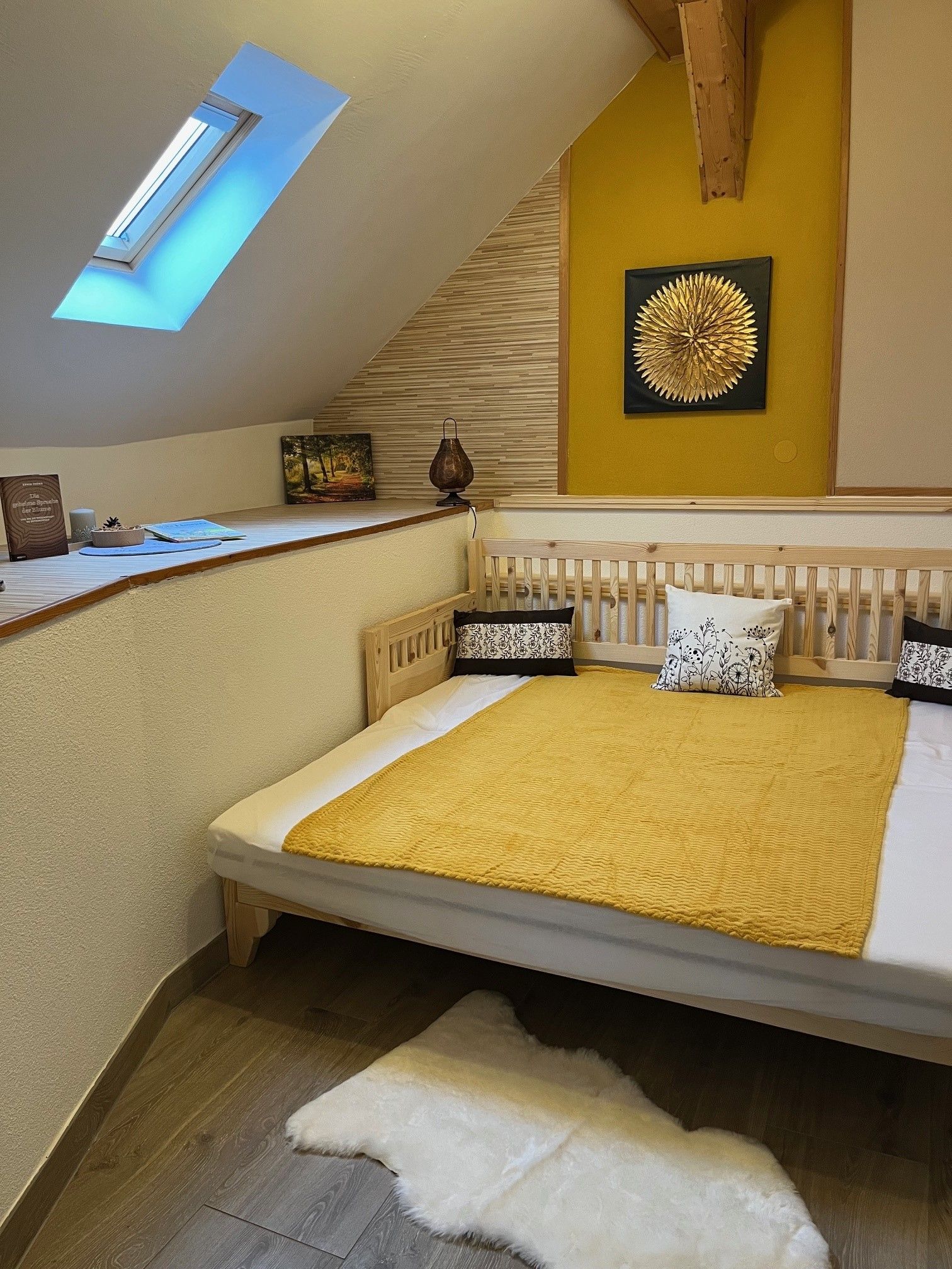 Gemütliches Schlafzimmer mit Dachfenster, gelber Wanddekoration und Holzbett.