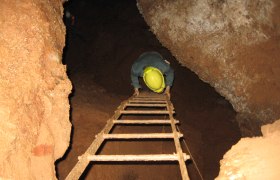 Person mit Helm klettert eine Leiter in einer Höhle hinunter.