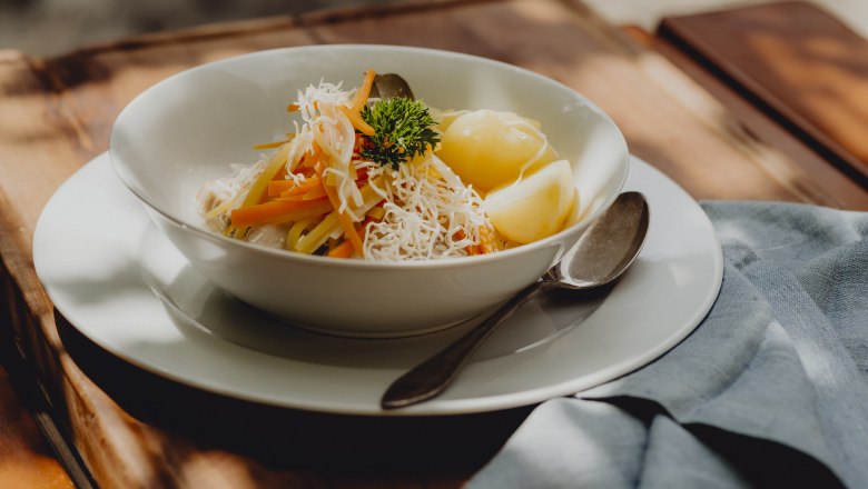 Ein Teller mit Krenfleisch, Wurzelstreifen und Salzerdäpfeln, garniert mit Petersilie, auf einem Holztisch.