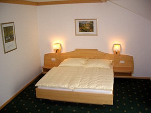 Ein einfach eingerichtetes Hotelzimmer mit einem Doppelbett, zwei Nachttischlampen und Bildern an der Wand.