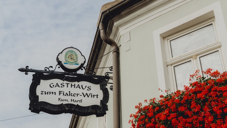 Schild des Gasthauses zum Fiaker-Wirt in Langenlois mit roten Blumen am Fenster.
