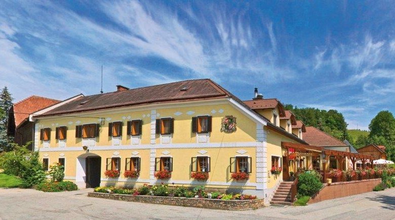 Traditionelles Gasthaus mit gelber Fassade, umgeben von gr&uuml;ner Landschaft und blauem Himmel.