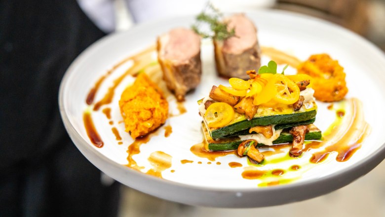 Ein Gourmetgericht auf einem wei&szlig;en Teller, kunstvoll angerichtet mit Fleisch, Gem&uuml;se und So&szlig;e.