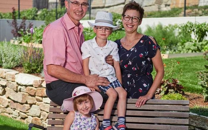 Familie Stradinger, © Familie Stradinger Eine Familie sitzt auf einer Bank im Garten, bestehend aus zwei Erwachsenen und zwei Kindern mit Hüten.
