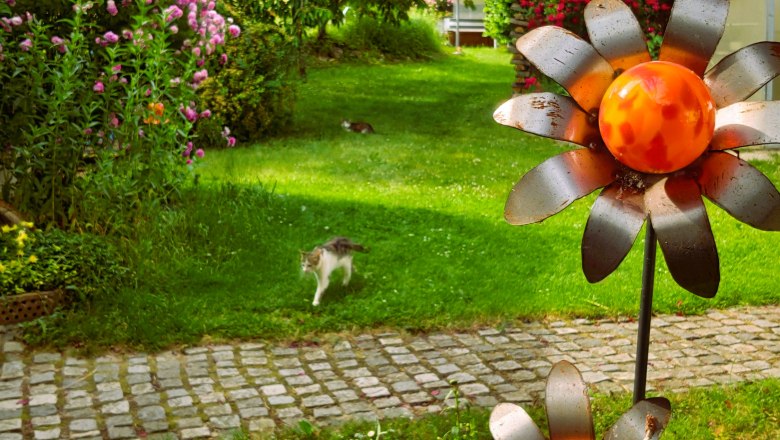 Ein Garten mit Blumen, einer Katze und Metallblumen.