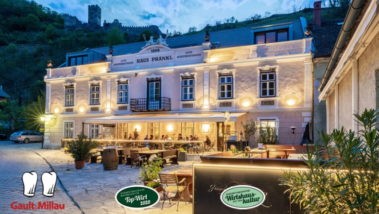 Abendaufnahme des Gasthofs Prankl mit beleuchteter Fassade und Gästen auf der Terrasse.