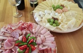 Zwei Platten mit Aufschnitt und Käse auf einem Holztisch, dekoriert mit Trauben und Tomaten.