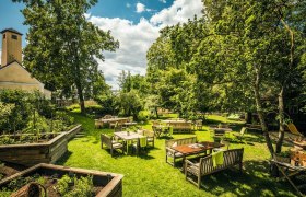 Garten mit sattem Grün und Holzmöbeln an Tischen, blauer Himmel