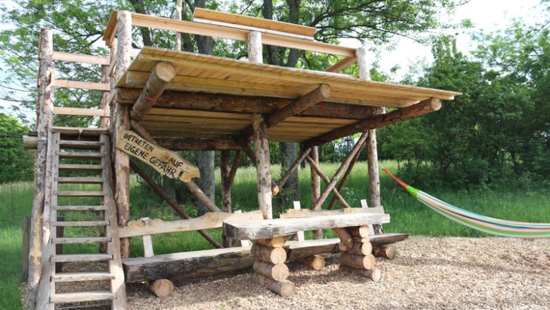 Holzplattform mit Tisch und H&auml;ngematte im Freien.