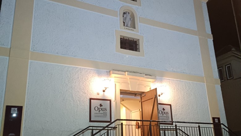 Eingang eines Geb&auml;udes mit Treppe und ge&ouml;ffneten T&uuml;ren, beleuchtet bei Nacht.