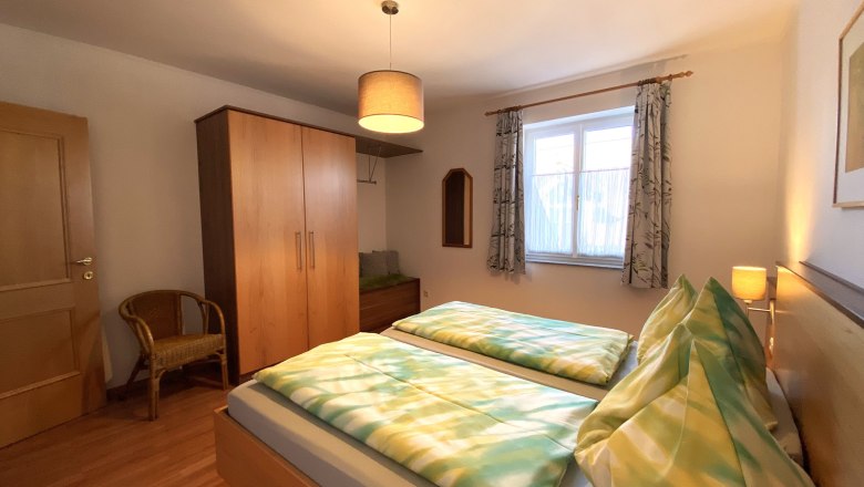 Schlafzimmer mit Doppelbett, Kleiderschrank, Stuhl und Fenster.