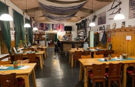 Gemütliche Gaststube mit Holztischen, Stühlen und Bar, dekoriert mit Fußballschals und rustikalen Elementen.