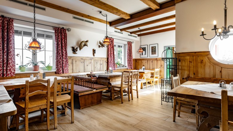 Gem&uuml;tlicher Gastraum mit Holzm&ouml;beln und roten Vorh&auml;ngen.