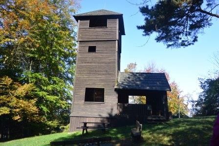 Holzturm im Wald mit blauem Himmel.