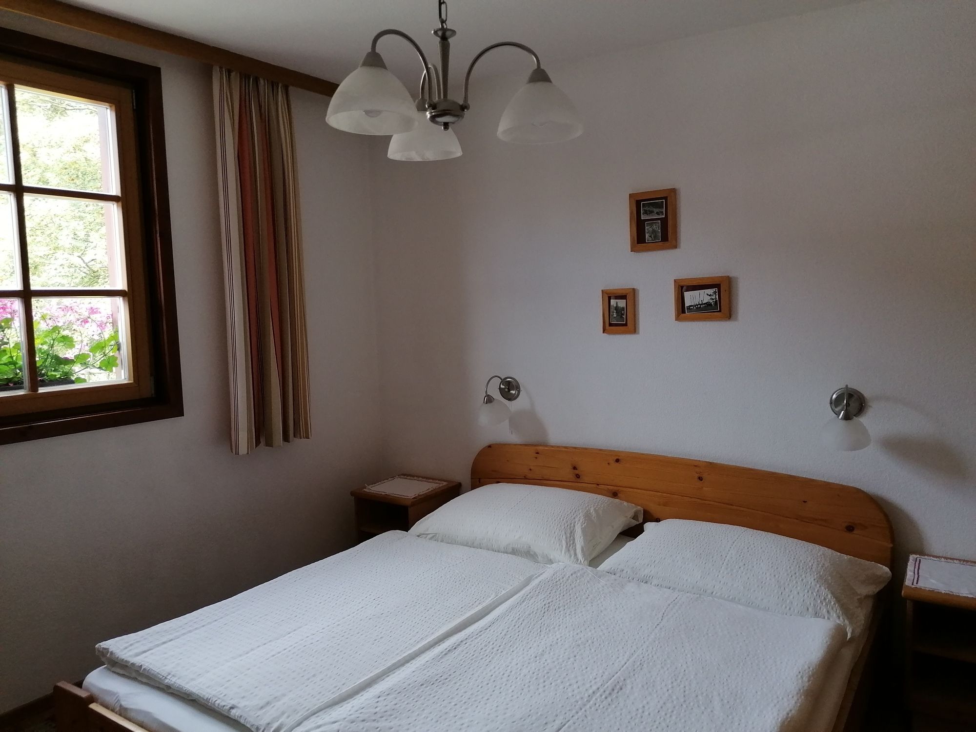 Gemütliches Doppelzimmer mit Holzmöbeln, einem Fenster mit Vorhängen und kleinen Bildern an der Wand.