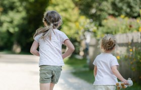 Zwei Kinder laufen auf einem Kiesweg in einem gr&uuml;nen Park.