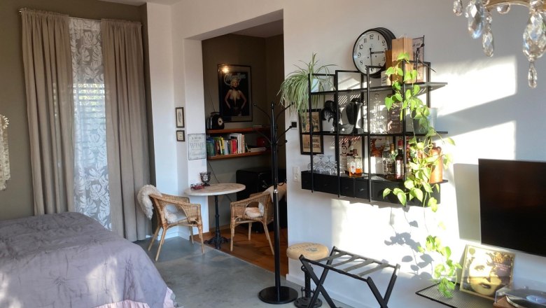 Gem&uuml;tliches Wohnzimmer mit Bett, Regal, Pflanzen und Wanddekoration.