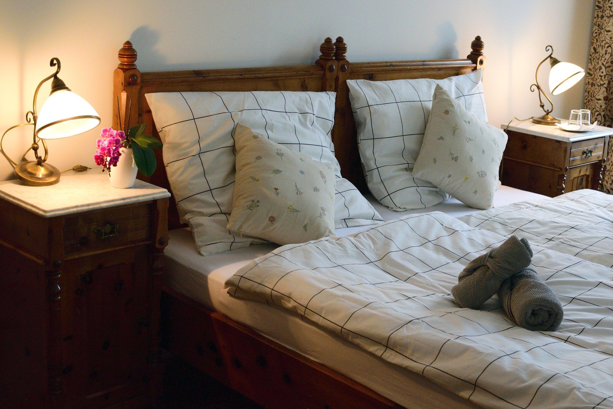 Gemütliches Doppelzimmer mit Holzmöbeln, Bett mit kariertem Bettzeug, Nachttischen und Lampen.