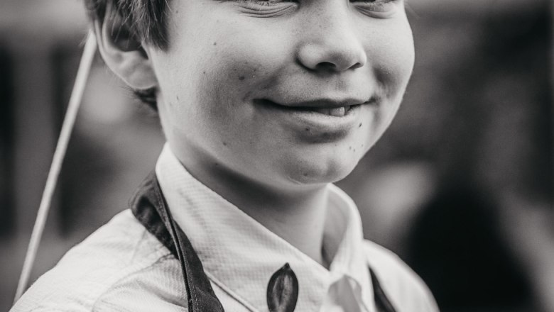 Ein Junge in einer Schürze mit der Aufschrift "Adam-Mühle" lächelt in die Kamera.