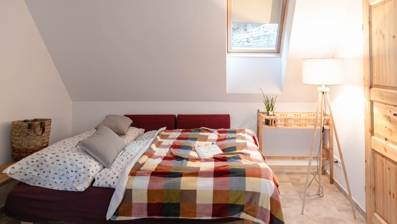 Gem&uuml;tliches Schlafzimmer mit Bett, bunter Decke und Leselampe.