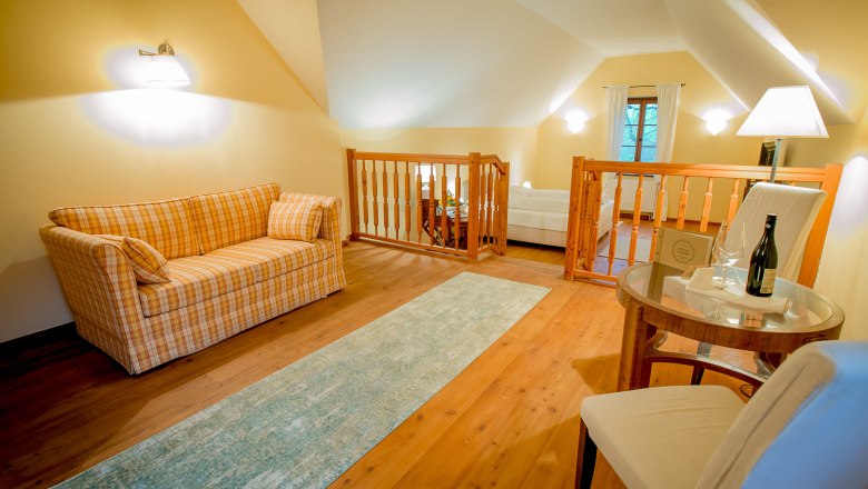 Gem&uuml;tliches Zimmer mit Sofa, Tisch und Stuhl, Holzboden und Gel&auml;nder.