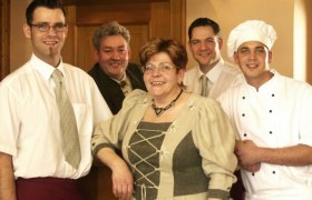 Fünf Personen in traditioneller Kleidung und Kochuniform posieren lächelnd in einem Raum.