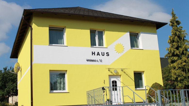 Gelbes Haus mit der Aufschrift 'Haus' und einer Sonne auf der Fassade.
