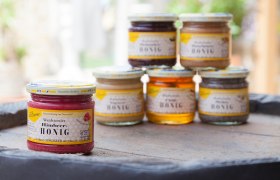 Verschiedene Honiggl&auml;ser auf einem Tisch, im Vordergrund Himbeer-Honig.