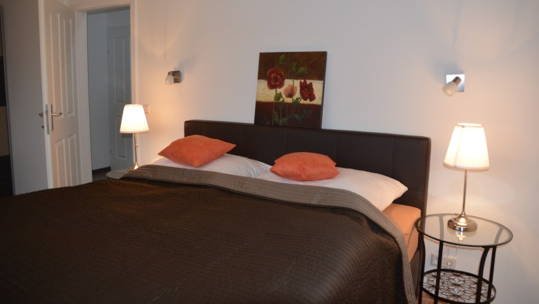 Ferienwohnung, © Familie Herrmann Schlafzimmer mit Doppelbett, zwei Nachttischlampen und einem Gemälde an der Wand.