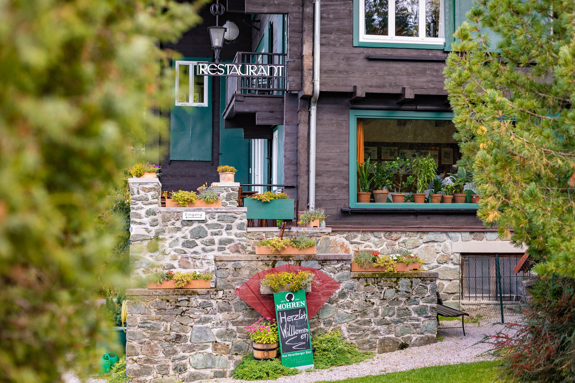 Außenansicht eines Restaurants mit Steinmauer und Pflanzen.