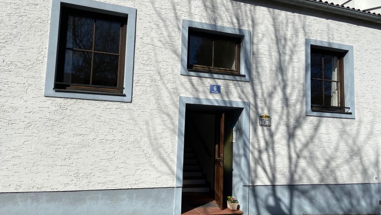 Eingang eines wei&szlig;en Geb&auml;udes mit blauen Fensterrahmen und T&uuml;rrahmen.