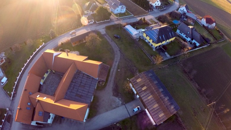 Luftaufnahme eines Dorfes mit H&auml;usern, Stra&szlig;en und Feldern bei Sonnenuntergang.