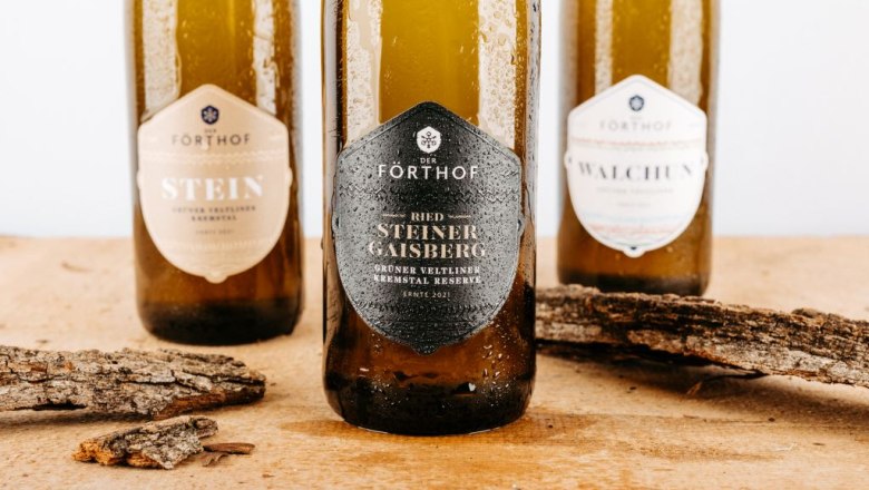 Drei Weinflaschen der Marke Förthof auf einem Holztisch mit Rindenstücken.