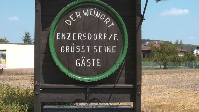 Holztafel in Enzersdorf an der Fischa mit Begr&uuml;&szlig;ungstext und Hinweis auf Heurigenbetrieb.